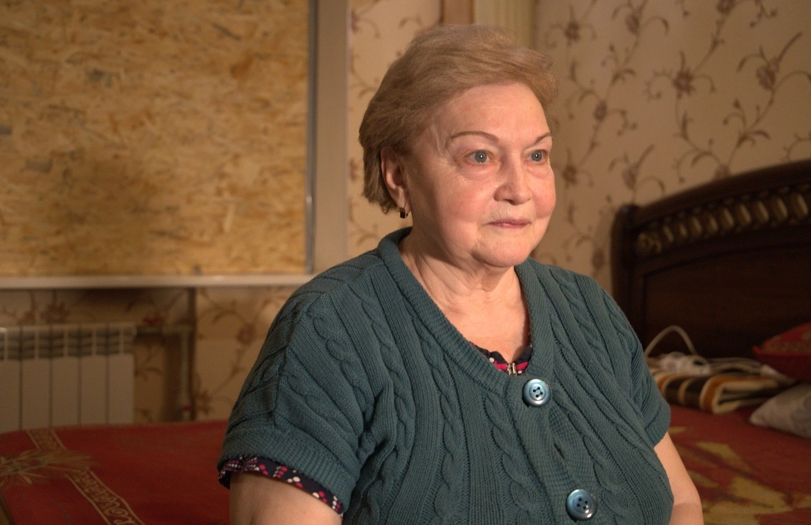 A woman sits on the edge of a bed staring into the distance