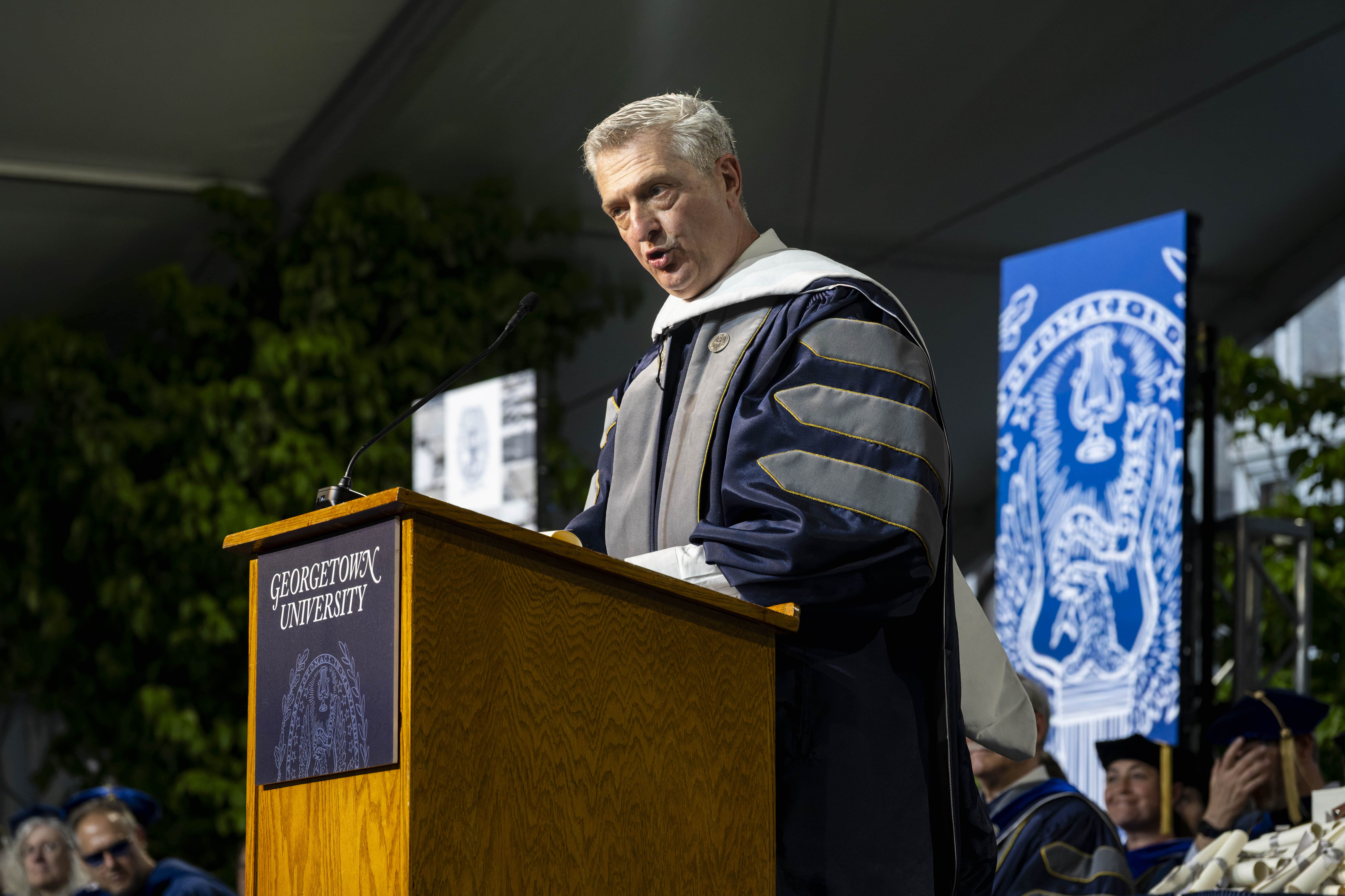 A man wearing ceremonial robes speaks at a lectern on stage