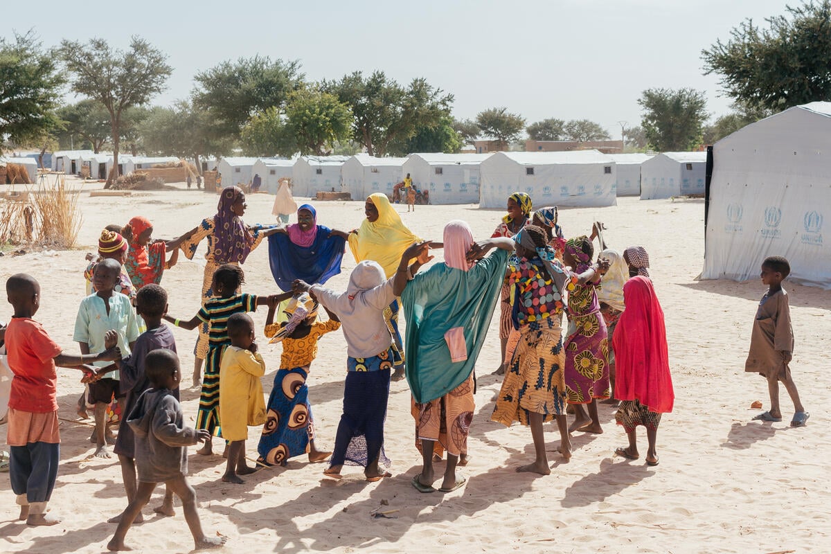 A group of Nigerian refugees play outside, with UNHCR tents in the background.