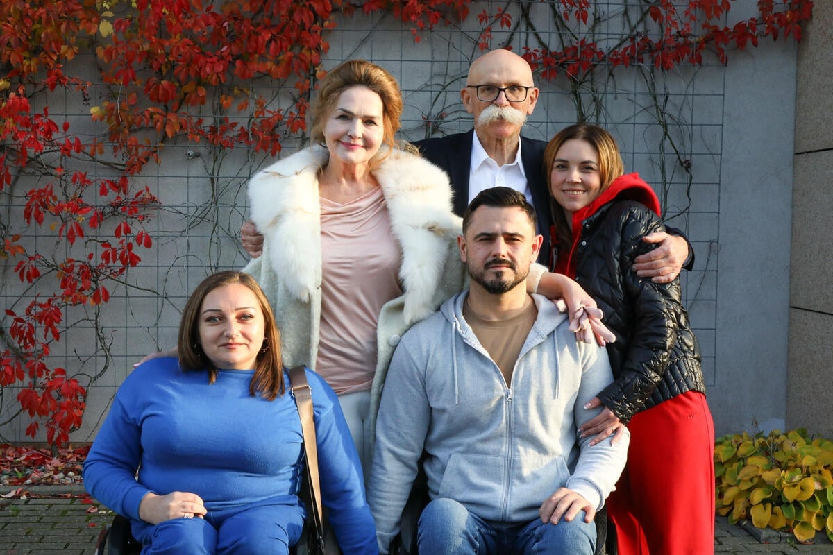 Five people pose for a group photo in front of a plant-covered wall.