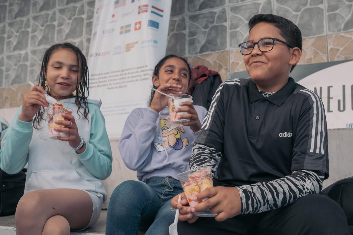 Three children laughing while eating dessert outside