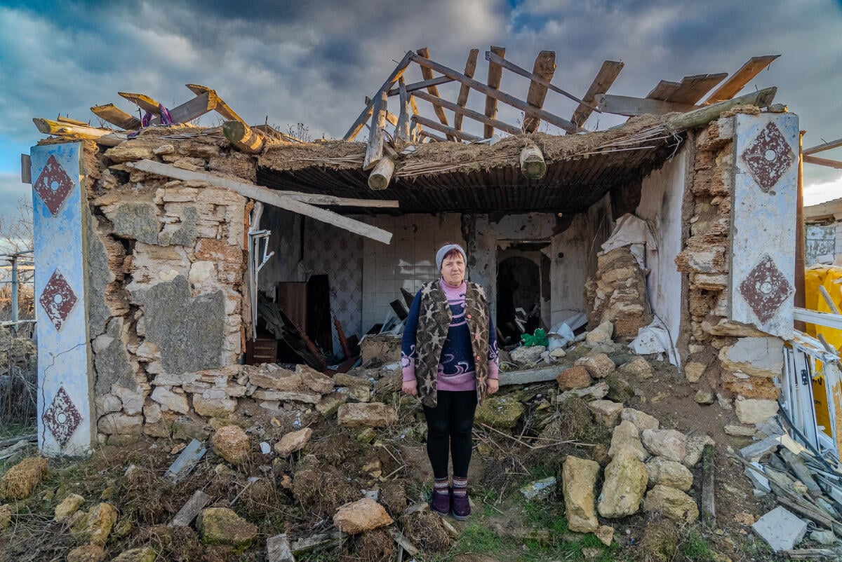 A woman stands near the remains of her house