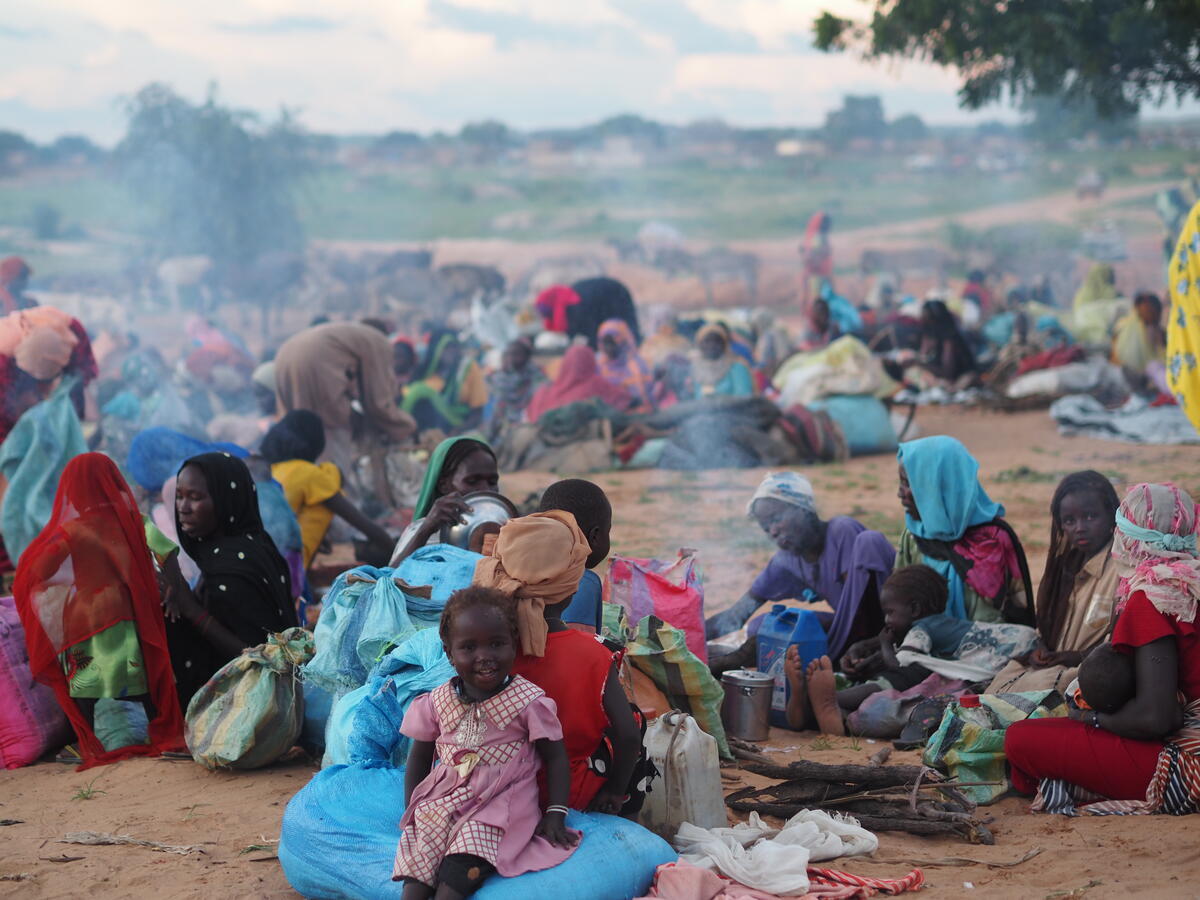 Women and children sit on the ground with their belongings.