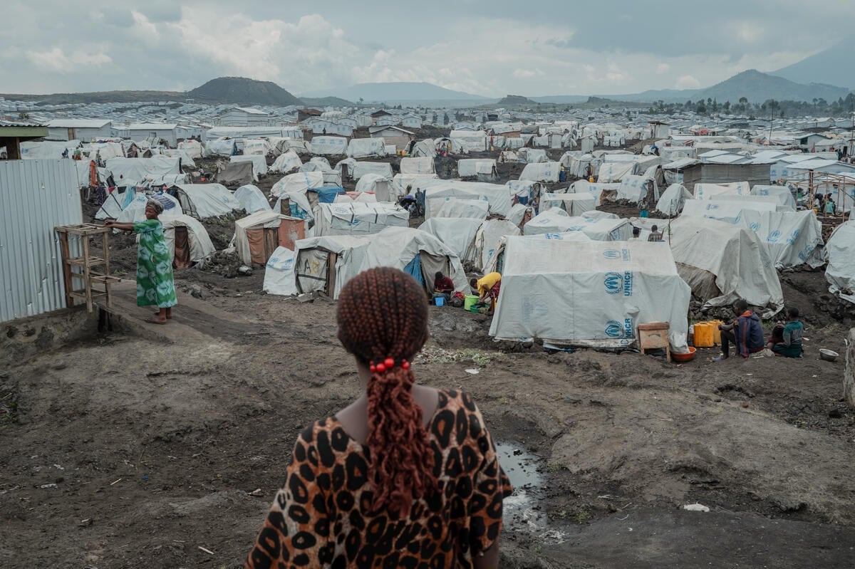 A rear view of a woman standing on muddy ground in front of hundreds of tents stretching to the horizon.