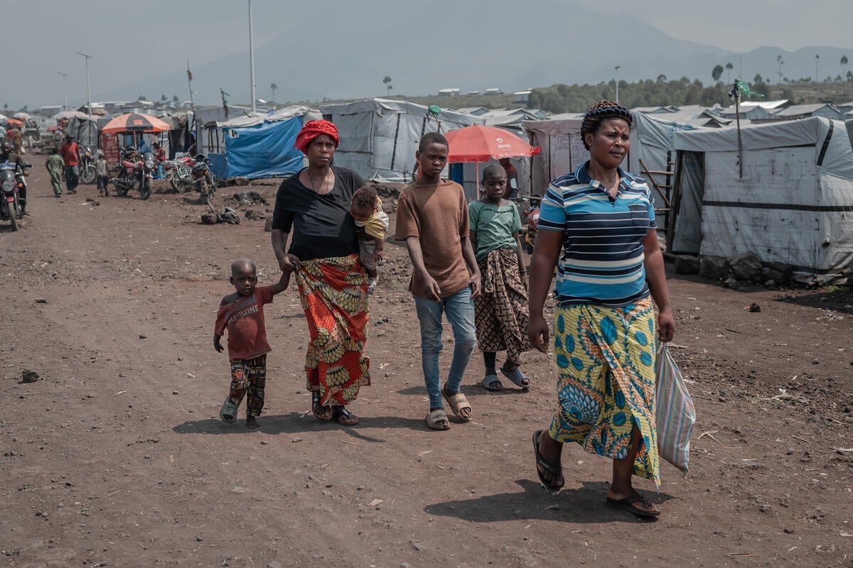 A woman walks with four children down the main thoroughfare of a camp behind another woman.