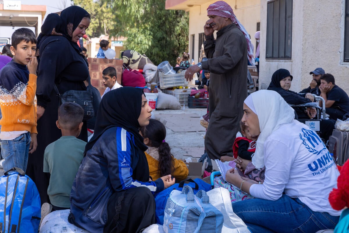 Syrian and Lebanese people sit on the ground in groups at a border crossing.
