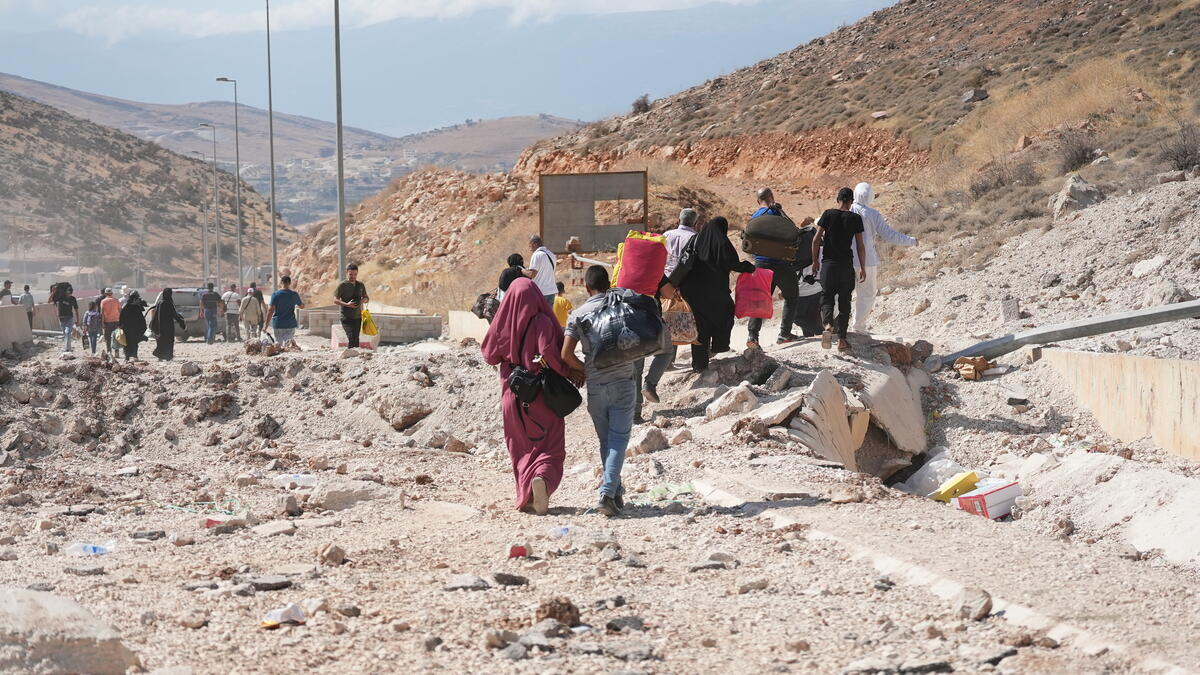 People carry their belongings down a rubble-strewn road with hills on either side