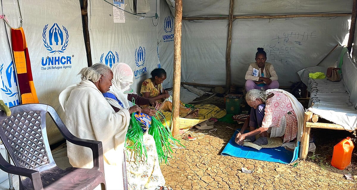 Several women sit inside a UNHCR tent and craft woven items