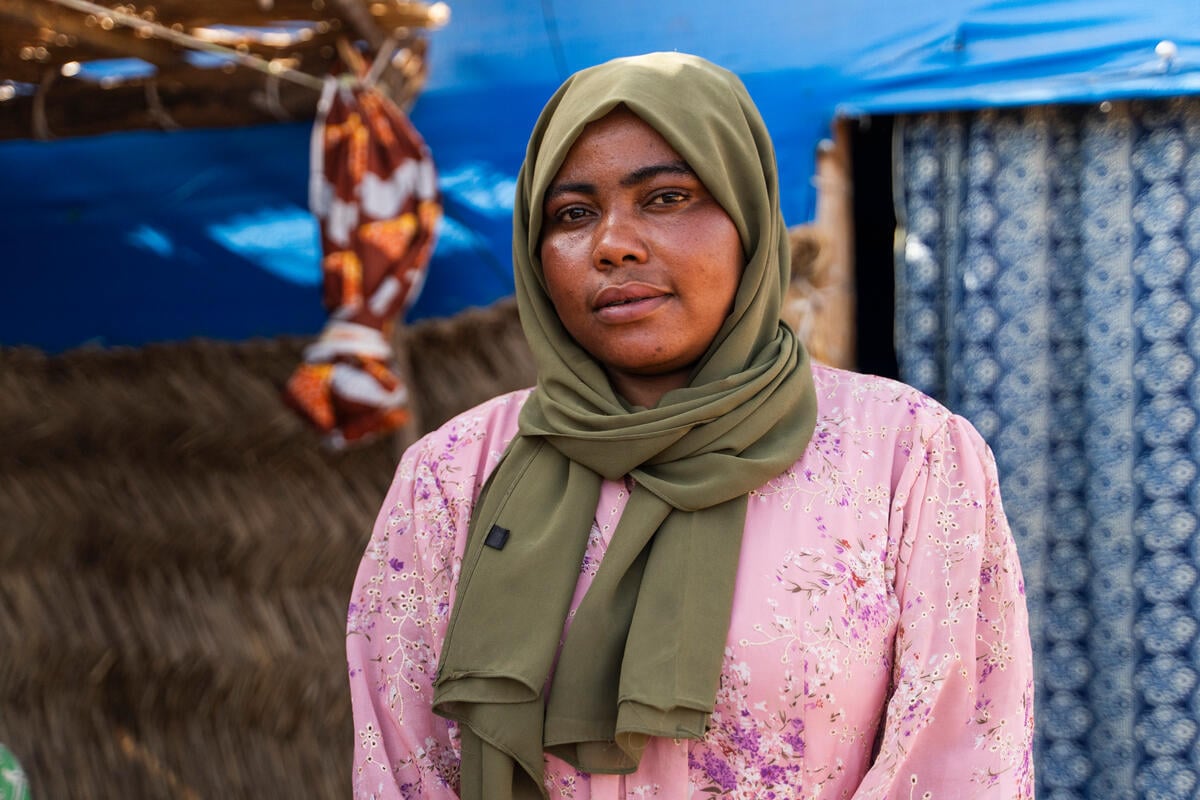 A portrait of a woman wearing a green headscarf standing in front of a shelter.