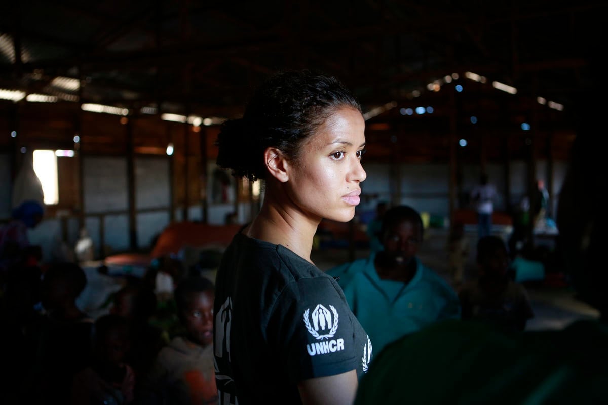 Gugu Mbatha-Raw stands in a room, wearing a UNHCR black t-shirt.