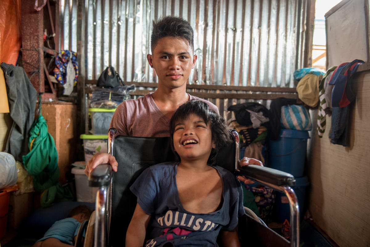 A young man kneels behind a boy who sits in a wheelchair.