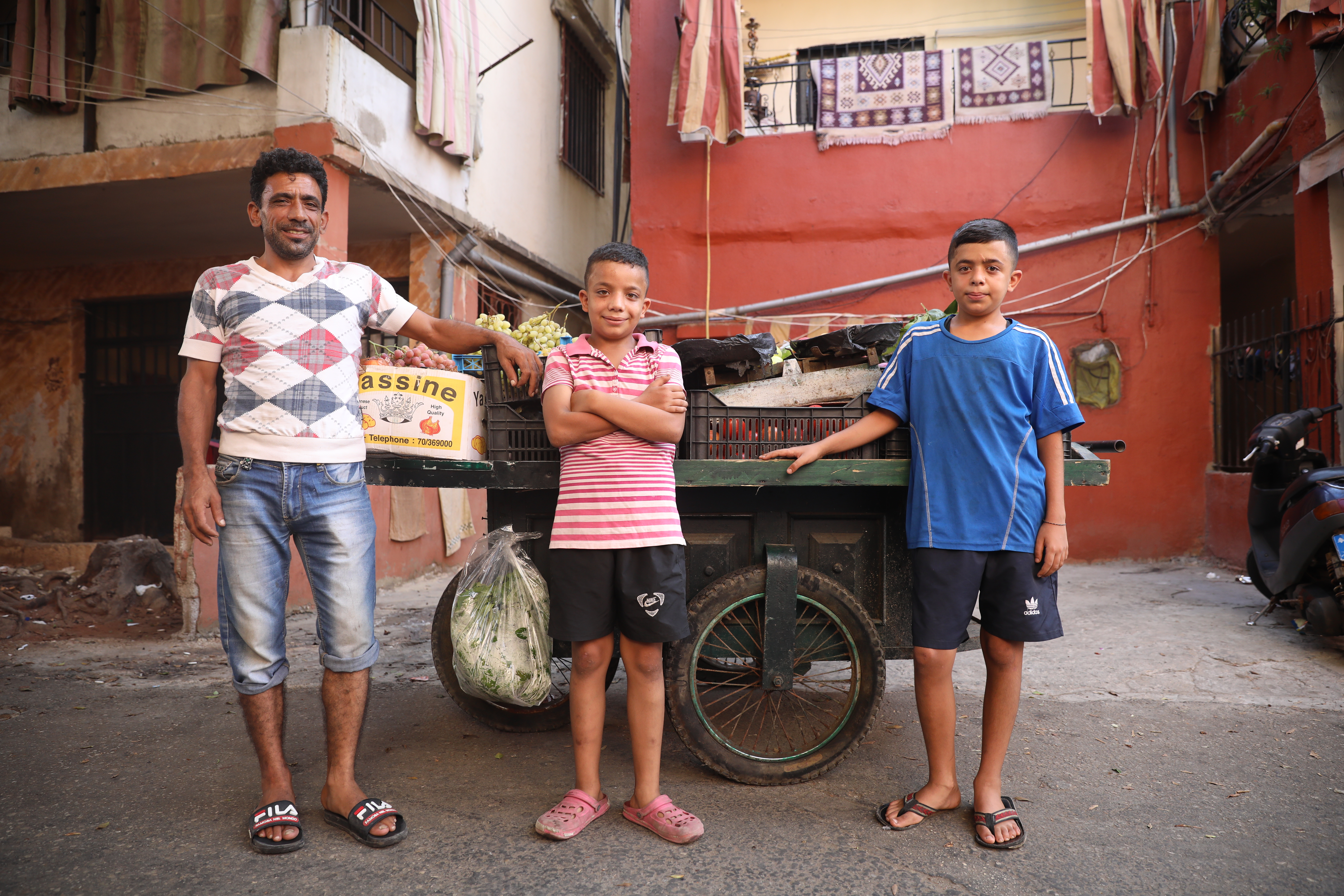 UNHCR UN Refugee Agency - Thirteen-year-old Gaith, a Syrian refugee, stands beside his father's fruit and vegetable cart in Beirut with his dad Samer Mohammed Ameno, 42, and brother Mohammed, 12.