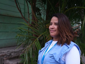 Mujer con chaleco azul de ACNUR y plantas al fondo