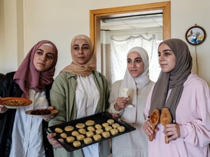 Four young women wearing headscarves hold up a tray of cookies.