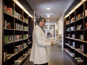 A woman in a lab coat stands between stacks of books in a library.