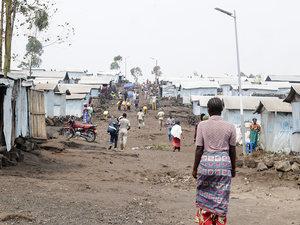 People in ones and twos walk over the undulating dry ground through a camp for internally displaced people 