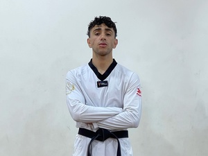 A man wears a white Taewkondo uniform with a black belt