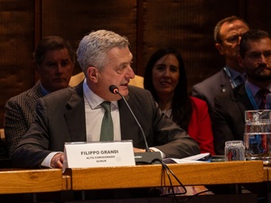 Filippo Grandi speaking at a desk with a microphone, a name placard in front of him and other people behind him.