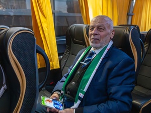 A man sits on a bus wearing a suit and scarf and holding a mobile phone