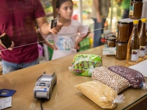 A man stands next to a young girl at the counter of a grocery store holding out a payment card to purchase bags of dried beans and pulses