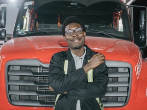 A man leans against the front a big, red truck.