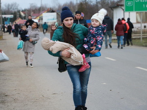A young woman walks along the side of a road carrying a toddler and a baby in her arms 