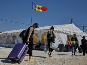 People carrying bags and pulling suitcases walk towards a large tent with a Moldovan flag flying above it
