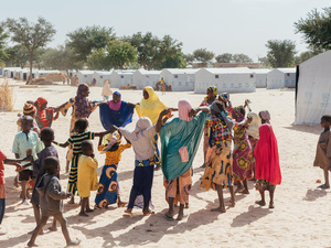 A group of Nigerian refugees play outside, with UNHCR tents in the background.