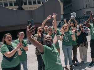 A group of smiling, cheering people take a selfie in Chicago at World Refugee Day celebrations