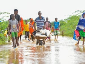 A man pushes a handcart containing a young child and his belongings through floodwaters accompanied by other family members.