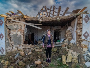A woman stands near the remains of her house