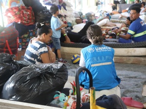 A UNHCR worker squats on the floor alongside refugees and their belongings in a temporary shelter