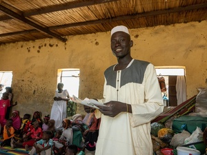 A young man holds some documents in a crowded room.