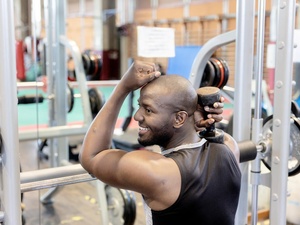  A man leans on a weight-lifting machine while holding a weight in one hand.