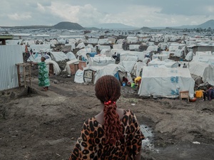 A rear view of a woman standing on muddy ground in front of hundreds of tents stretching to the horizon.