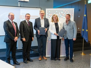 Four men and one woman stand looking at the camera while holding up two documents