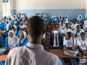 A teacher pictured from behind, in front of a classroom of secondary-aged Sudanese refugees.