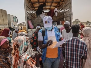 A UNHCR staff member checks documents in a group of people standing at the back of an open truck.