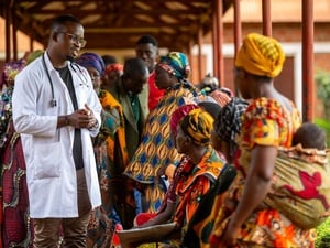 A clinician in a lab coat meets with a group of people outside.