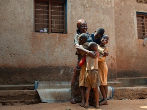 A Burundian woman hugs four of her children standing outside a building with a huge smile on her face