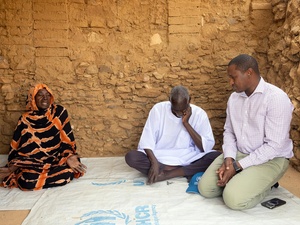 Mamadou Dian Balde sits on the floor, speaking with two Sudanese refugees.