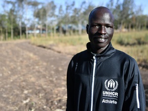 Portrait of a man in a UNHCR-branded tracksuit top standing on a dirt road.