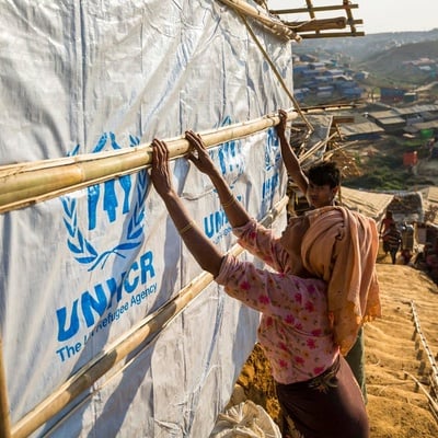 Two refugees build a shelter with bamboo poles and tarpaulins