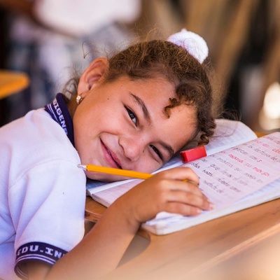 A girl smiles while leaning on her open notebook in a classroom at a school in Colombia.