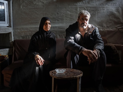 A woman and a man sit on a sofa in the living room of a tented structure.