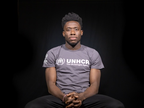 Alphonso Davies sitting in chair, wearing UNHCR t-shirt 