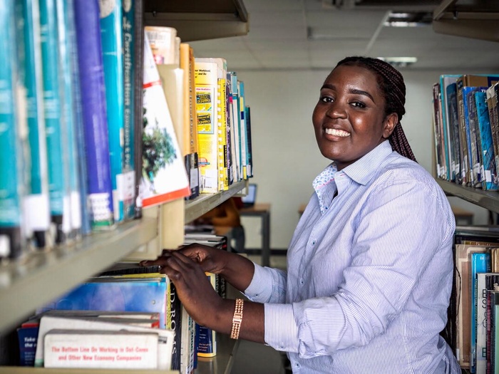 A young woman stands smiling in front of a bookshelf in a library