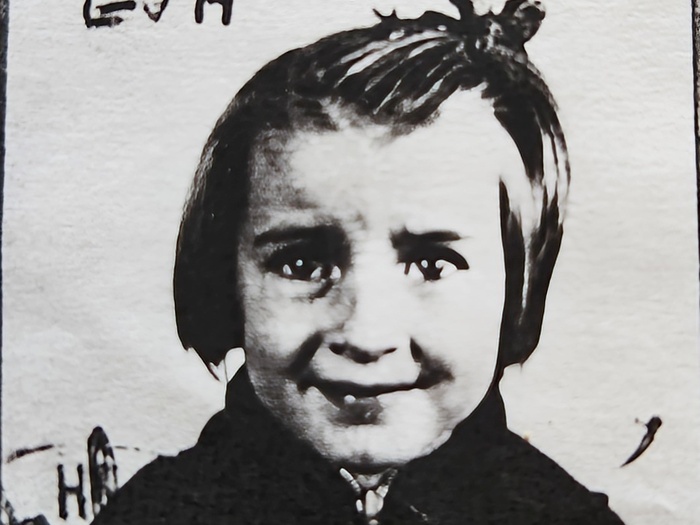 Grainy black-and-white photo of a smiling young girl in an overcoat with writing on the background
