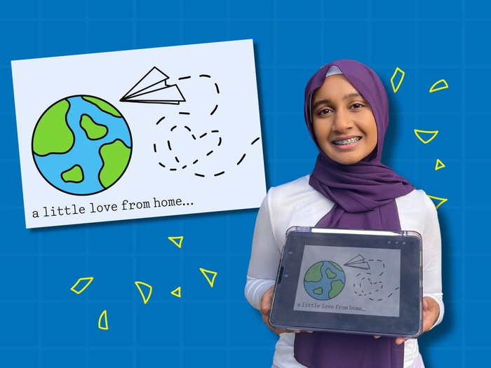 Afya holds up her design, a drawing of a paper airplane flying towards a globe. The trail of the paper plane makes the shape of a heart.