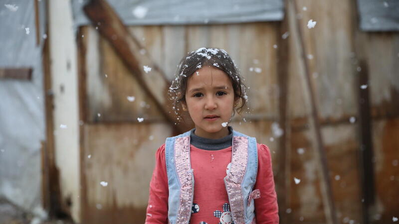 Hadeel, a young Syrian refugee girl stands in front of her tent while it snows, in Lebanon. 
